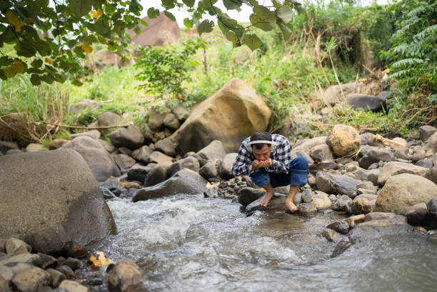 man drinking fresh water from a river while hiking in the forest
