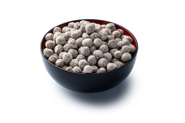 Uncooked black tapioca pearls in a black bowl, close up on white background. Studio shot. High angle view.