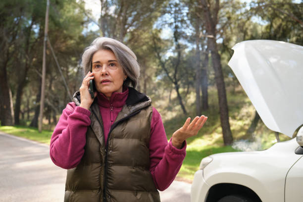 istock Senior woman making a phone call with a broken down car and open hood 2194389870