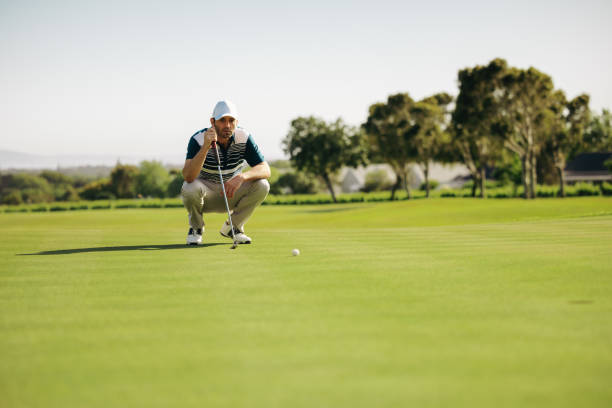 istock Crouching golfer on putting green aiming at golf ball on a lush green course under a clear sky, balancing on a club 2194390076