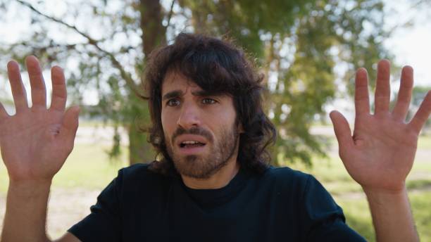 istock Scared Man Raises His Hands Before Receiving Theft From A Criminal In a Park 2194392217