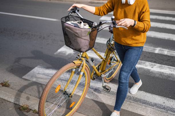 Young woman walking with her yellow bicycle on a crosswalk, carrying groceries in the basket