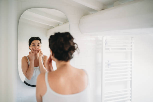 istock Woman applying moisturizer on face in bathroom mirror 2194400365