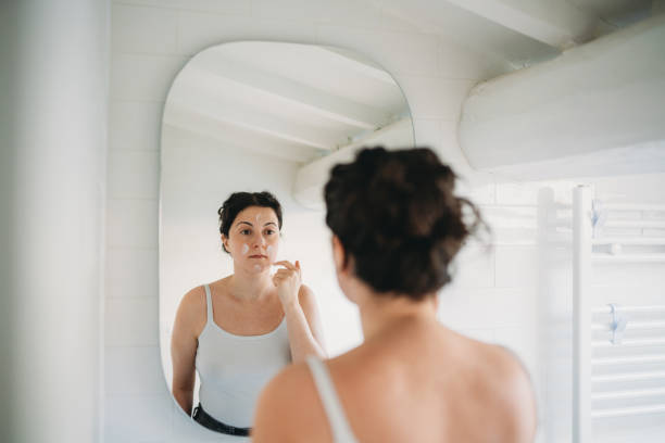 istock Woman applying moisturizer on face in bathroom mirror 2194400378