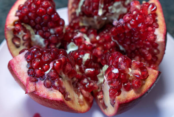 Close-up of a fresh ripe pomegranate fruit lying on a white plate, cut into beautiful slices.