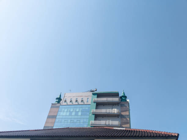 A contemporary buildings facade rises against a serene, cloudless sky. Its clean lines and teal accents create a tranquil, minimalist aesthetic.