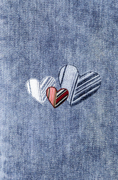 Light blue denim background with felt heart. Vertical blue color denim jeans fabric texture with heart-shaped textile patch. Valentine's day denim backdrop. Copy space for text