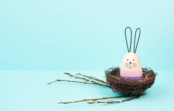 istock Easter bunny or rabbit sitting in a bird wicker nest, willow branches, wooden egg, spring holiday, brown and blue color 2194413983