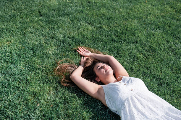 istock pretty young woman lying on green grass 2194415442