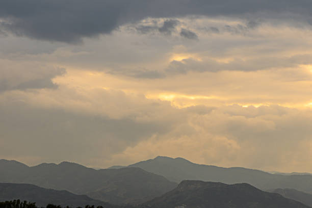 Golden rays peek through clouds above stunning mountain silhouettes, creating a tranquil and enchanting atmosphere.