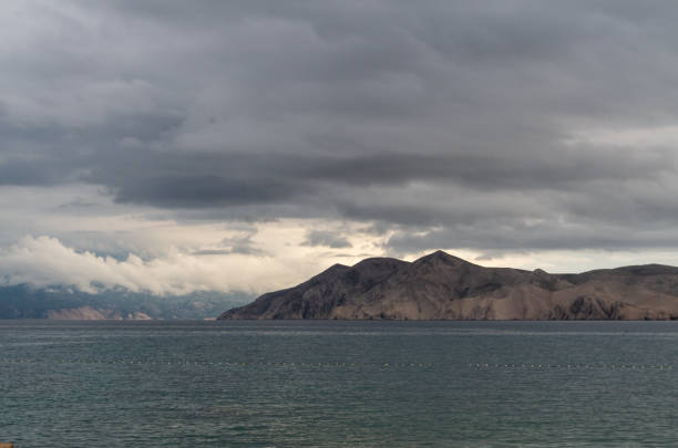 A captivating seascape featuring a rugged island against a dramatic sky. The image captures the raw beauty of the Croatian coastline, with its rocky shores and turbulent waters. Perfect for travel, nature, and landscape projects.