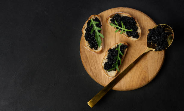 istock Three pieces of crispy bread with luxurious black caviar and fresh arugula, served on round wooden board 2194426013