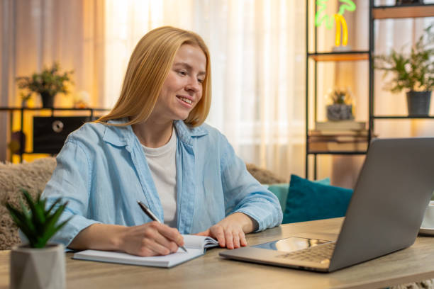 istock Young woman studying at home video laptop lesson focus, notes in notebook, attentive learning moment 2194430185