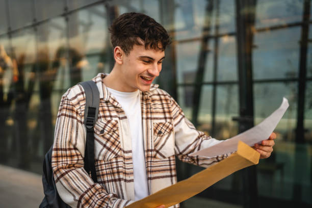 istock Young adult man student open and read files from envelope outdoor 2194430963