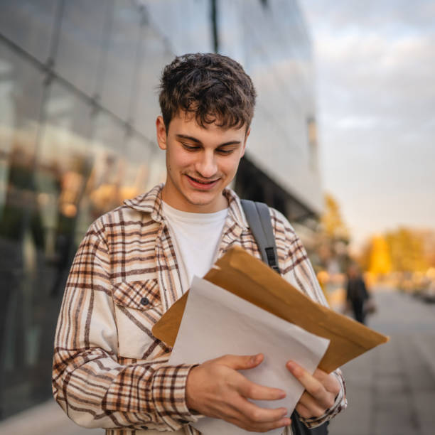 istock Young adult man student open and read files from envelope outdoor 2194432020