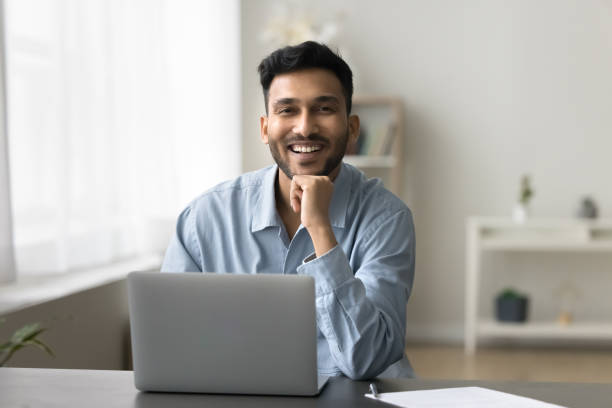 istock Indian man sits at desk with laptop looking at camera 2194432296