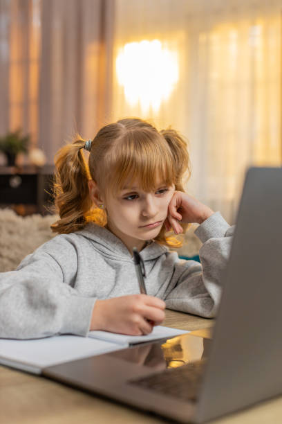 istock Tired young girl doing homework at table with laptop writing in notebook and showing lazy expression 2194436635