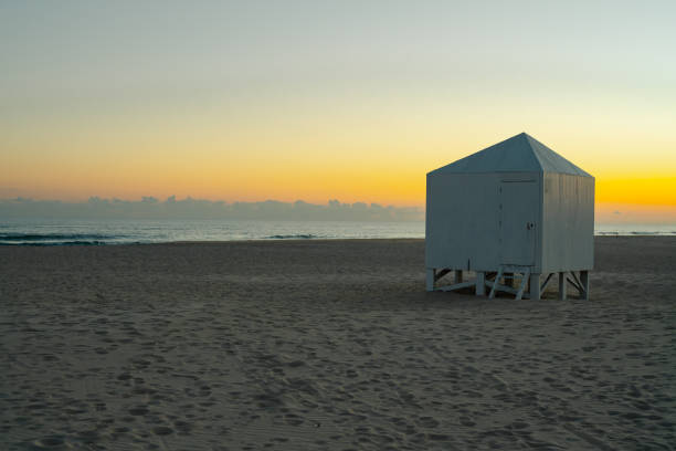 Solitary beach hut illuminated by the soft hues of a serene sunset.