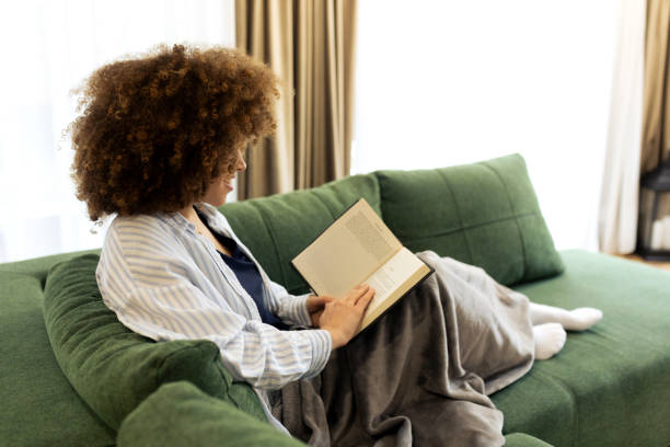 istock Beautiful Young woman sitting on a sofa and reading a book 2194439682