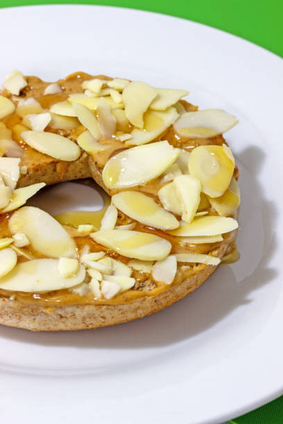 Whole grain breakfast bagel with sliced almonds and manuka honey over peanut butter spread isolated closeup