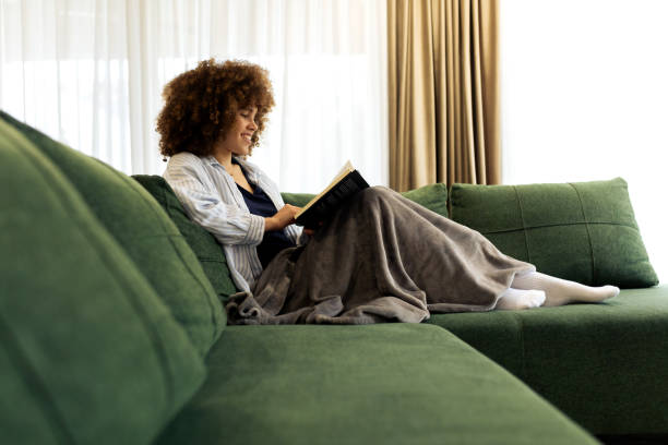 istock Beautiful Young woman sitting on a sofa and reading a book 2194443208