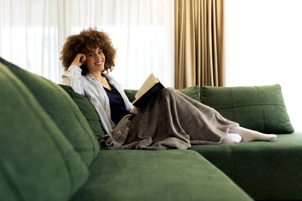 istock Beautiful Young woman sitting on a sofa and reading a book 2194443239