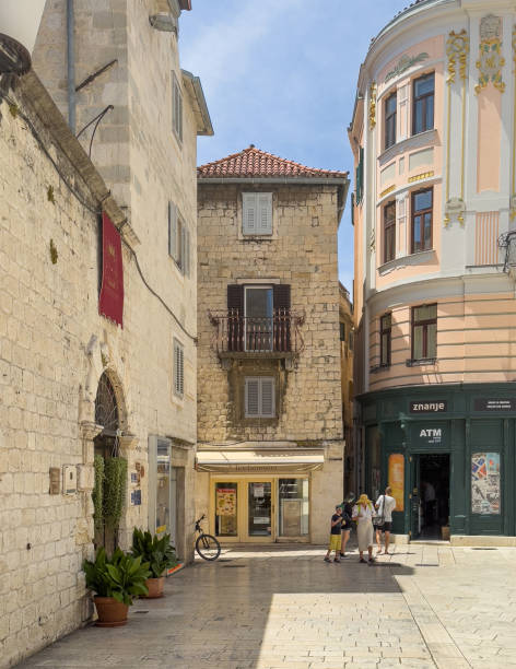Split, Croatia - July 1, 2024: Historic downtown. SW corner of people square with retail stores such as Optica Anda and Bonbonniere Kras. Judita Palace Heritage Hotel with the plants in front and the banner above