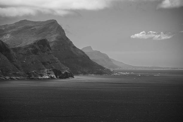 Monochrome landscape of rugged coastal cliffs and calm sea under a cloudy sky, capturing the serene beauty of nature.
