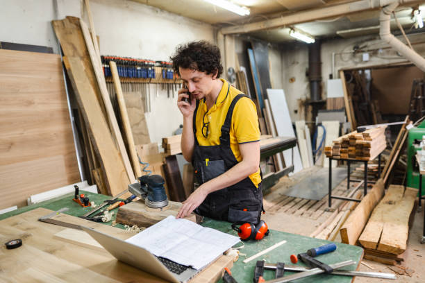 istock Carpenter talking on mobile phone and reading blueprint in workshop 2194447723