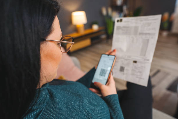 istock Woman scanning qr code from invoice on her smartphone at home 2194447925