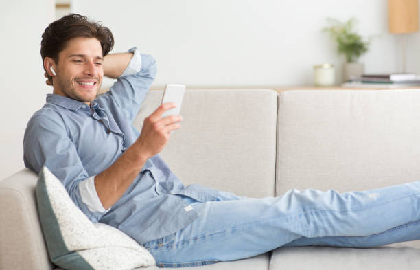 istock Young Man Relaxing on Sofa While Using Smartphone at Home in Casual Attire During the Day 2194454784