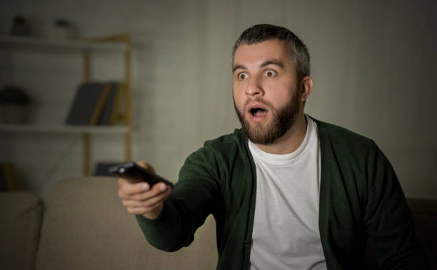 istock Man Expresses Shock While Watching Television at Home During Nighttime 2194458553