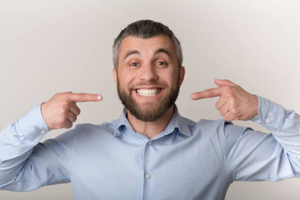 Man Shows Bright Smile With Thumbs up While Wearing a Light Blue Shirt Indoors