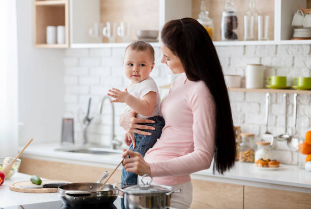 istock Mother Cooking in Kitchen While Holding Her Baby During the Day 2194458699
