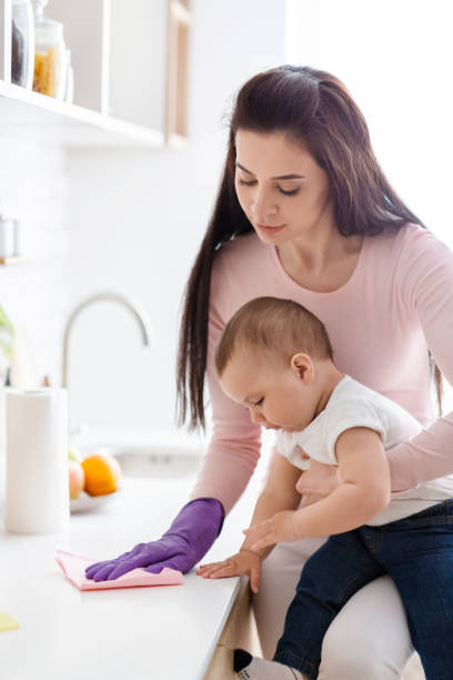 istock Mother Cleans Kitchen While Holding Baby in Her Arms During the Day 2194458716