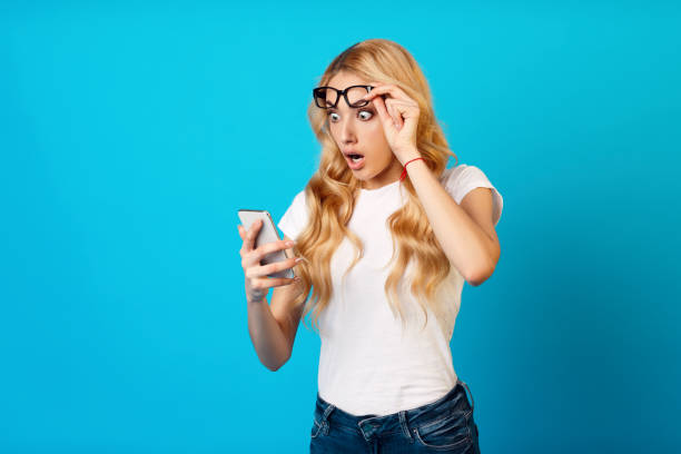 istock Young Woman Reacts in Surprise While Checking Her Smartphone Against a Bright Blue Background 2194461132