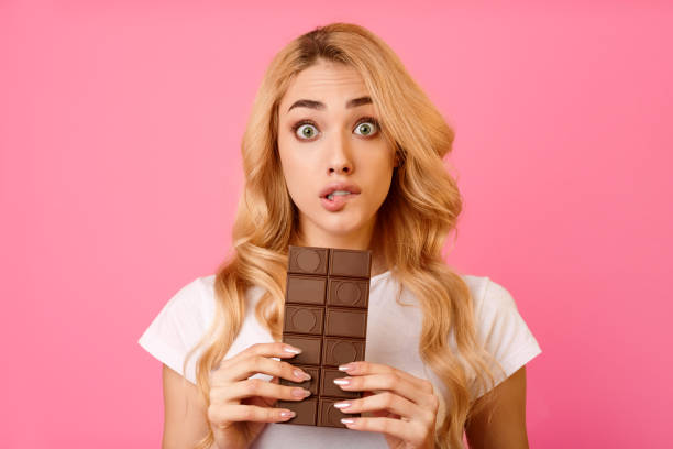 istock Woman Surprised While Holding Chocolate Bar Against a Pink Background 2194461192