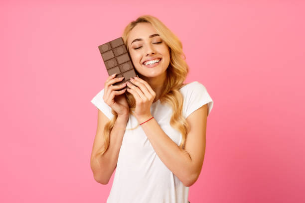 istock Woman Joyfully Holding a Chocolate Bar Against a Pink Background While Smiling Brightly 2194461211