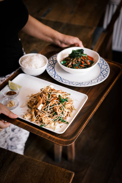 istock Authentic Thai Pad Thai Noodles and Stir-Fried Hot Basil with Vegetables Served with Steamed Rice on a Wooden Tray in a Cozy Restaurant Setting 2194478658