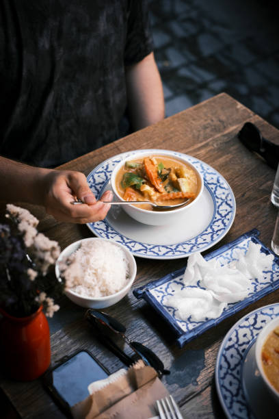 istock Thai Red Curry with Prawns Served with Steamed Jasmine Rice and Prawn Crackers on Blue-Patterned Plates in a Warm and Rustic Restaurant Dining Atmosphere 2194478736