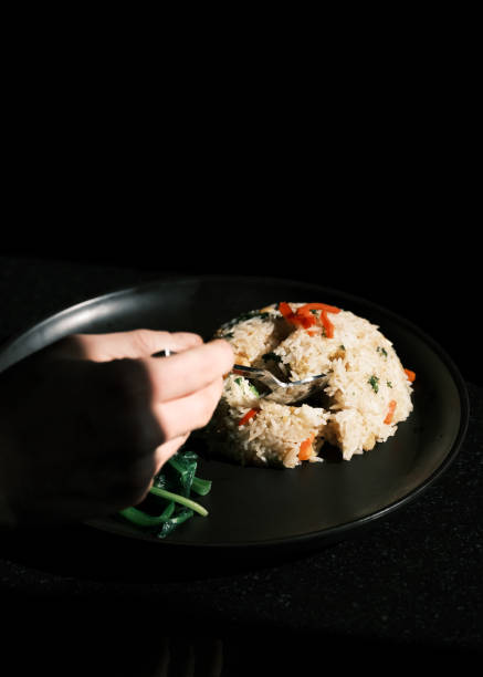 This image showcases a plate of Thai fried rice served with fresh vegetables, elegantly plated on a black dish. The dish highlights the harmony of stir-fried rice with a mix of colorful vegetables, reflecting the authentic flavors and simplicity of Thai culinary tradition. The dark background emphasizes the rich textures and vibrant colors of the meal, creating a visually striking composition.