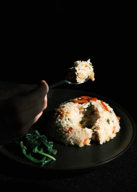 This image showcases a plate of Thai fried rice served with fresh vegetables, elegantly plated on a black dish. The dish highlights the harmony of stir-fried rice with a mix of colorful vegetables, reflecting the authentic flavors and simplicity of Thai culinary tradition. The dark background emphasizes the rich textures and vibrant colors of the meal, creating a visually striking composition.
