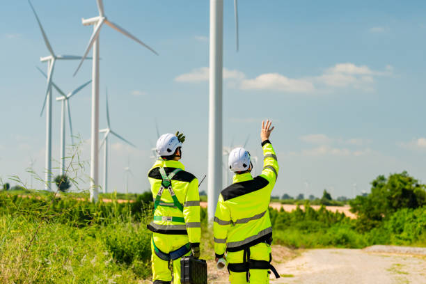 istock Two workers in bright safety gear inspecting wind turbines in a green landscape under a clear blue sky 2194486842