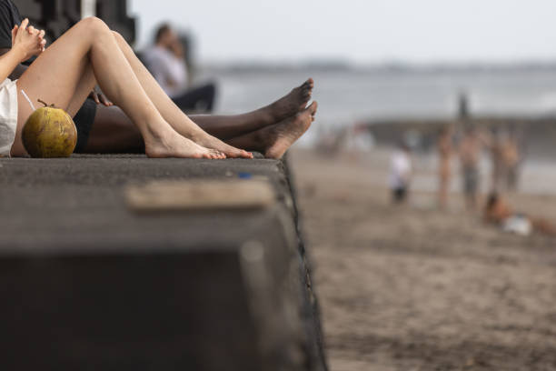 Mixed race couple is sitting on Canggu beach.\nBali Island - Indonesia.