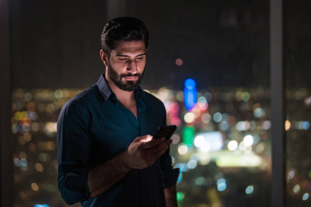 istock Young Arabic Male Engaged with Smartphone Against Riyadh Night View 2194497700