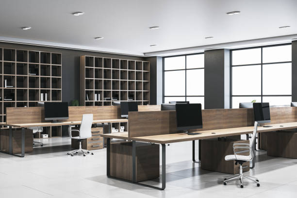 istock Modern office interior with wooden desks and computers, spacious and well-lit with large windows and shelves in the background. 3D Rendering 2194499367