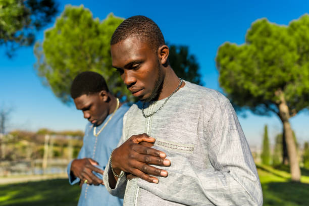 Two young senegalese men wearing traditional clothing are praying outdoors in a park during the holy month of ramadan