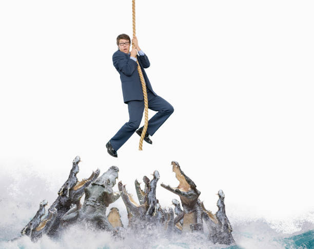 Businessman hangs on end of rope above snapping crocodiles, John M.Lund