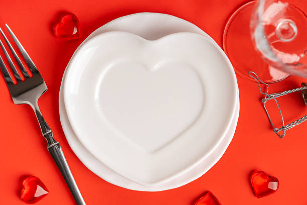 istock Overhead view of white heart shaped empty plate served on red table with fork and glass 2194507320