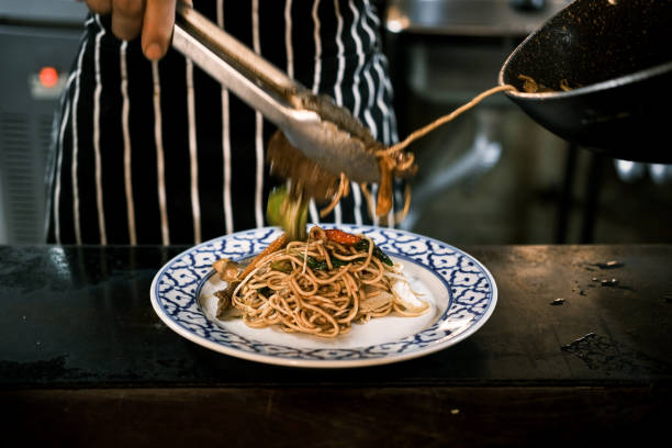 istock Stir-Fried Egg Noodles with Tender Beef, Fresh Vegetables, and Thai Spices, Served Hot on a Blue-Patterned Plate in a Traditional Thai Restaurant by a Skilled Chef in Apron 2194511325